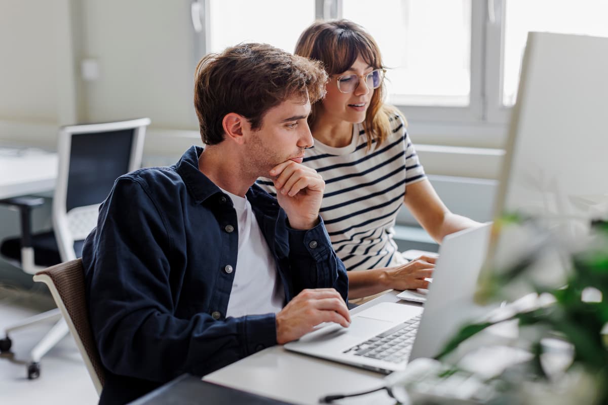 Deux collègues analysent les changements des cotisations patronales sur ordinateur dans un bureau moderne, dans le cadre de la réforme LFSS 2025