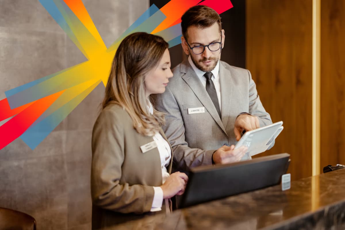 Deux réceptionnistes d’hôtel en uniforme discutent devant un ordinateur et une tablette, illustrant la gestion des ressources humaines et la collaboration dans le secteur hôtelier
